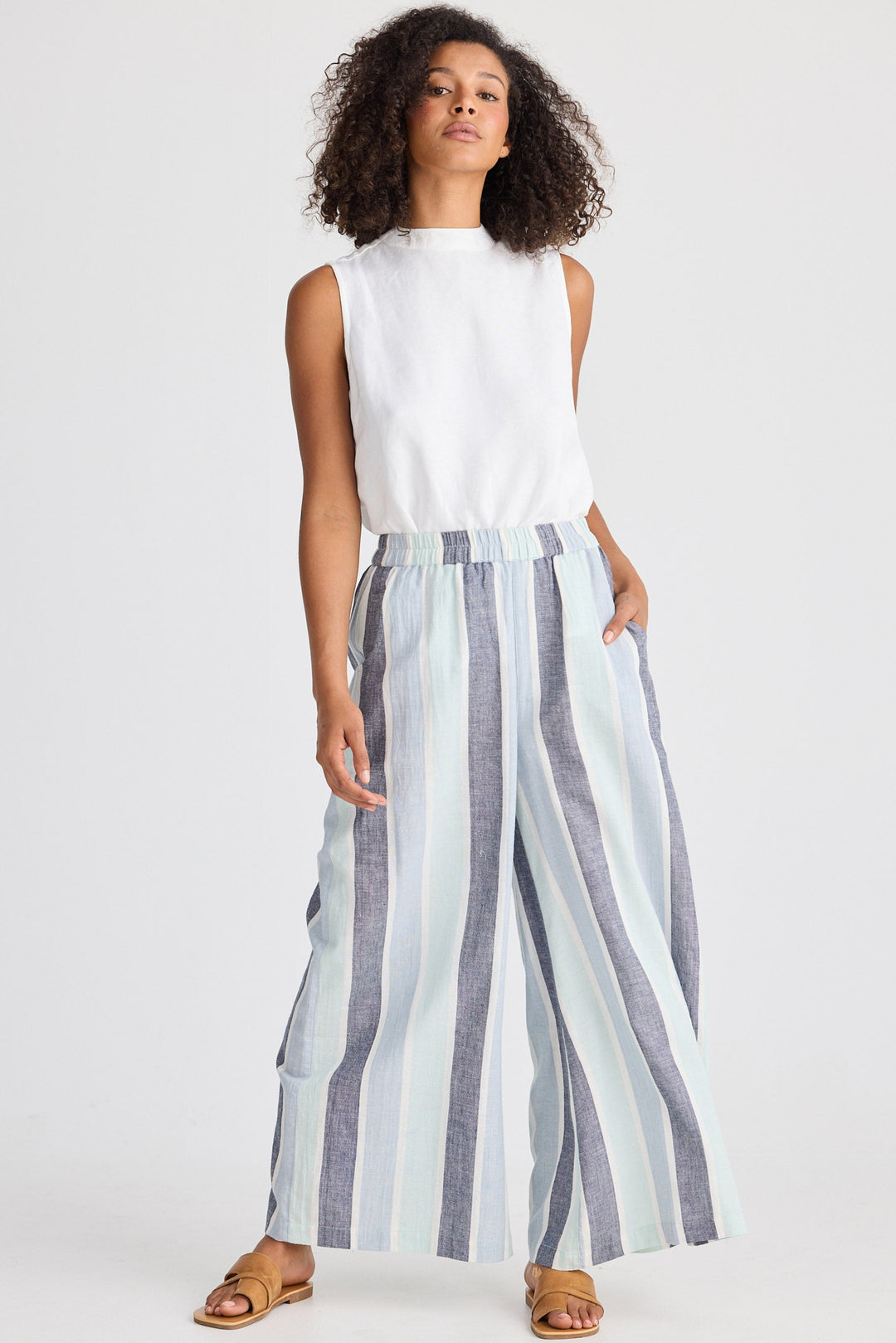 Woman wearing a white sleeveless top and striped wide-leg pants on a white background