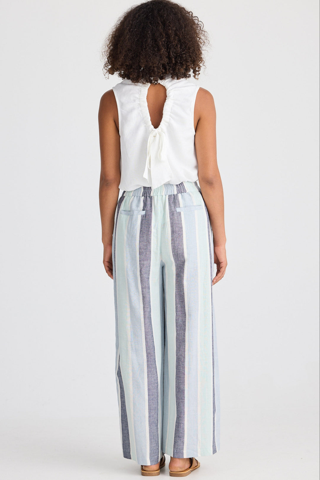 Woman wearing a white sleeveless top and striped pants on a plain background