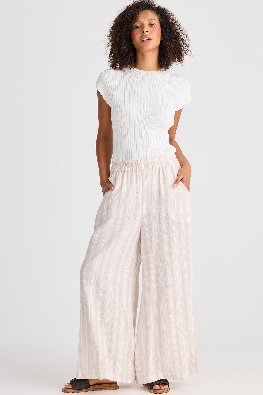 Woman wearing a white top and beige striped wide-leg pants on a white background
