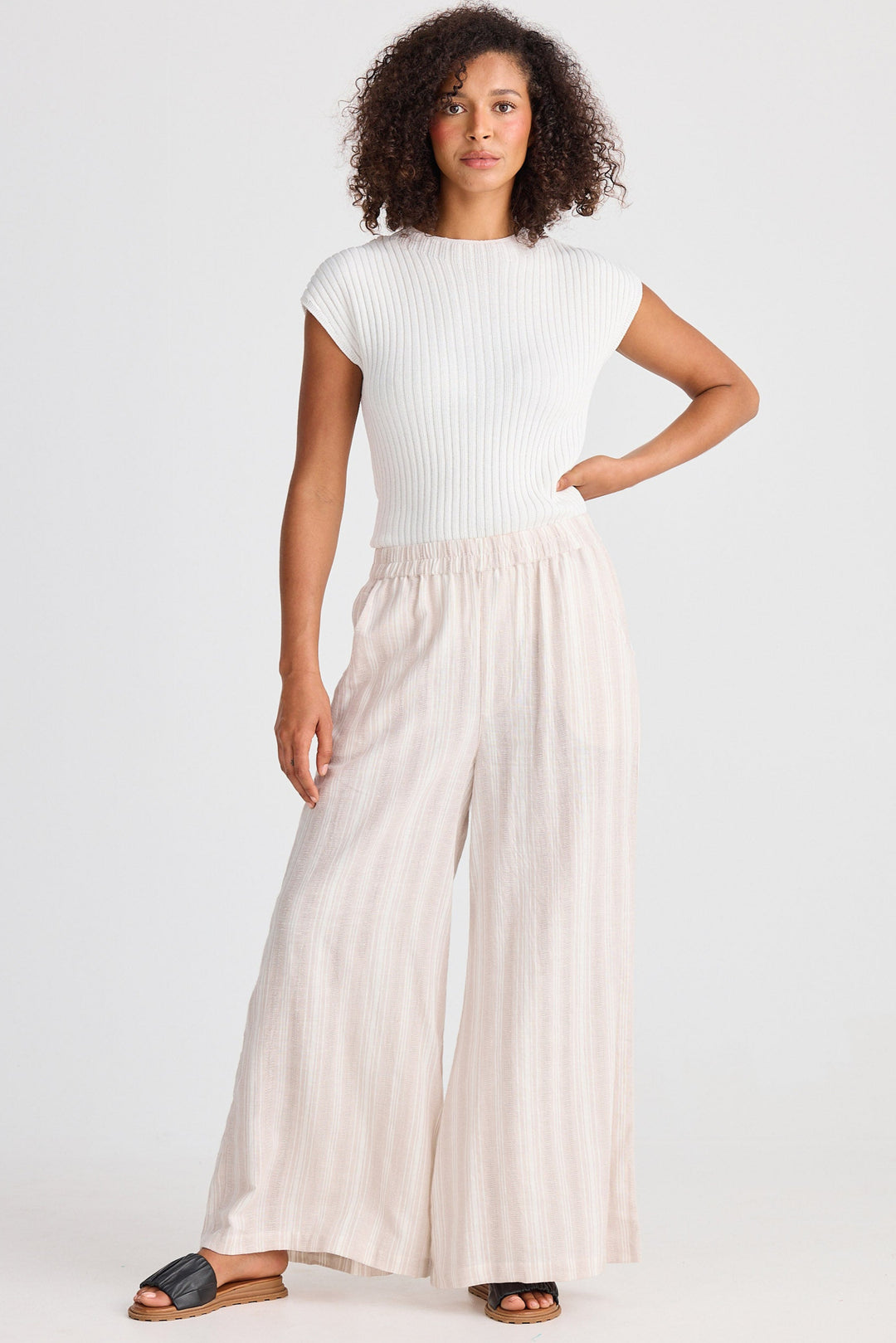Woman wearing a white top and beige striped wide leg pants on a white background
