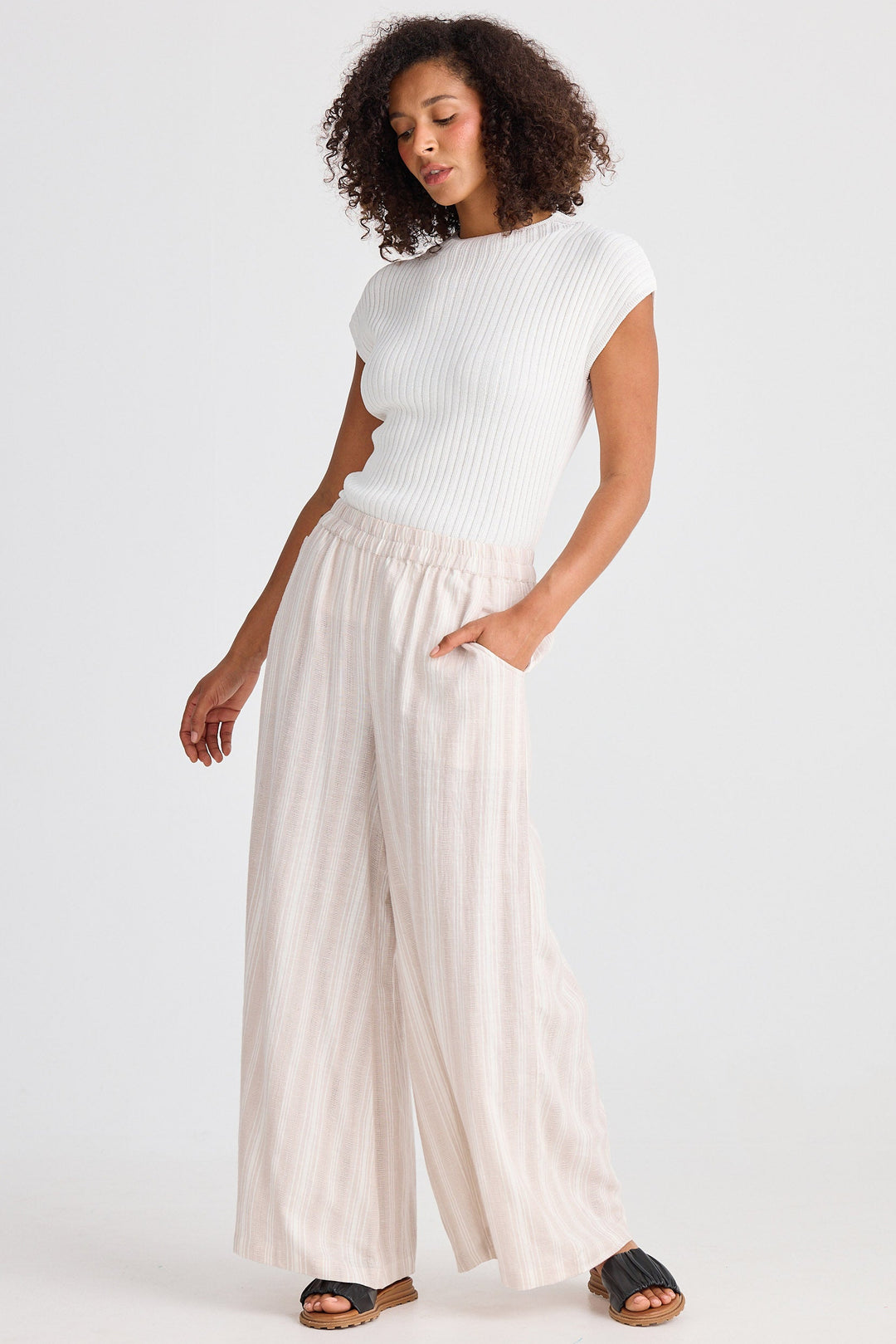 Woman wearing a white top and beige striped wide-leg pants on a white background