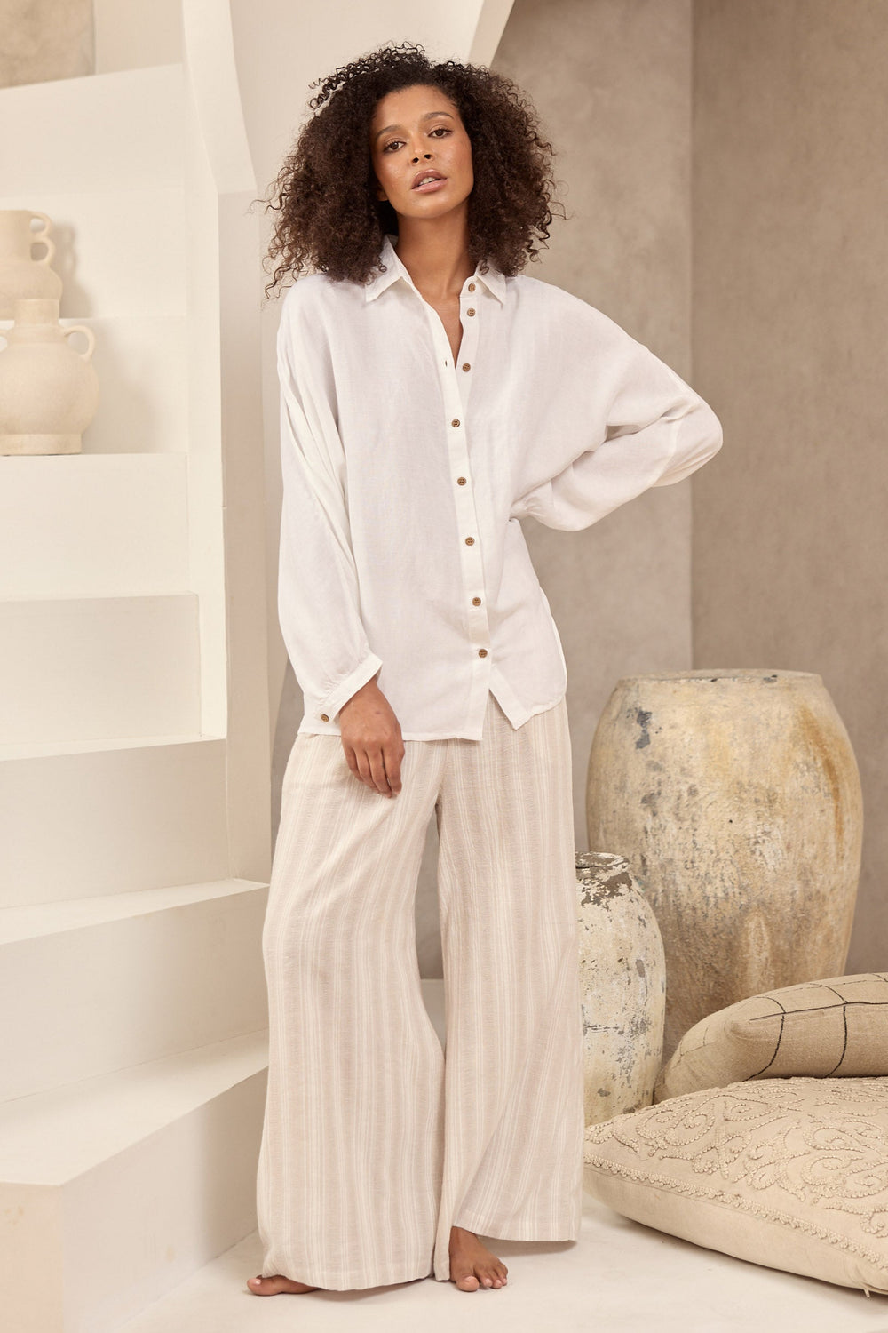 Woman in white shirt and light coloured striped pants standing in a minimalistic room with neutral decor.