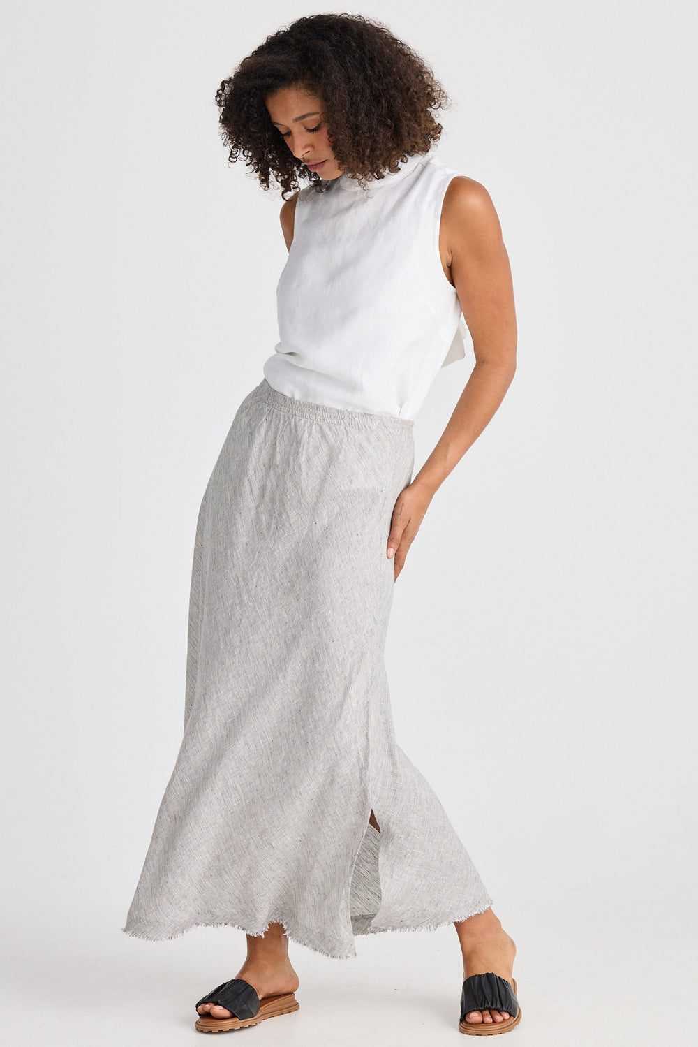 Woman wearing a white sleeveless top and light gray skirt on a white background