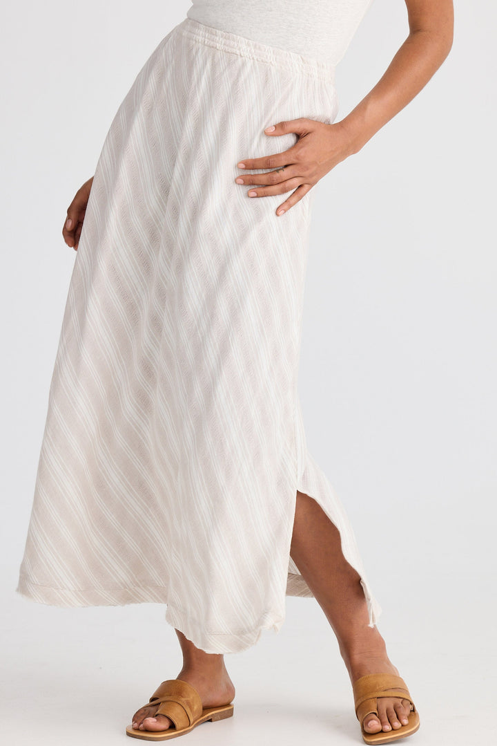 Person wearing a light striped skirt and brown sandals on a plain background