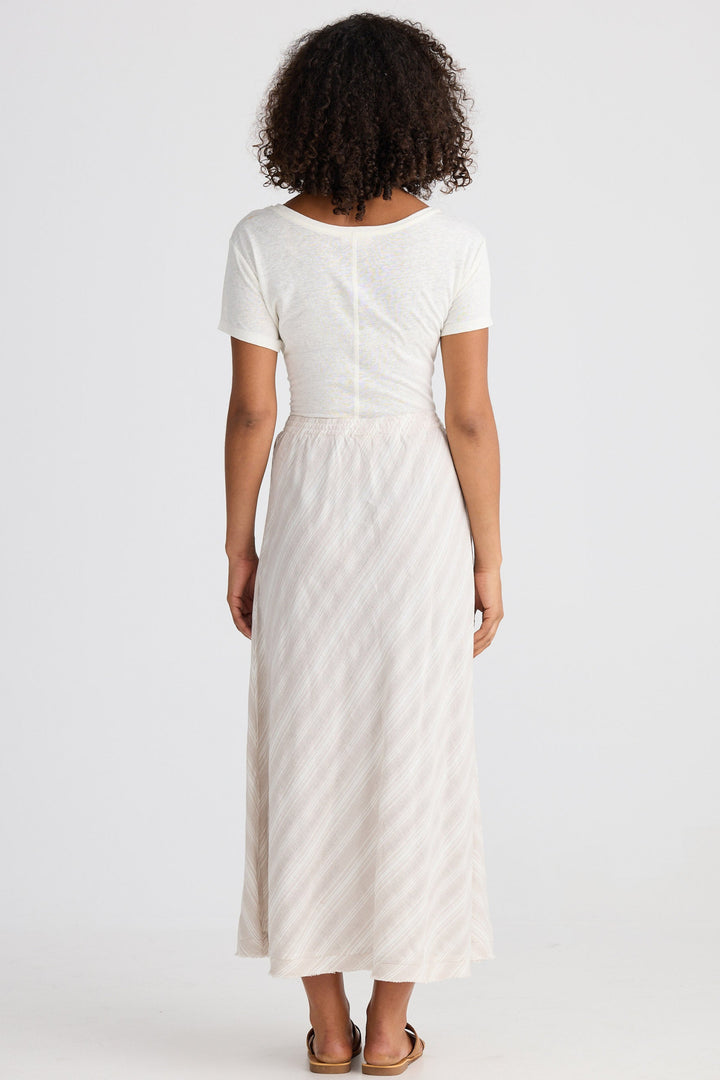 Woman wearing a white top and light striped skirt on a plain background