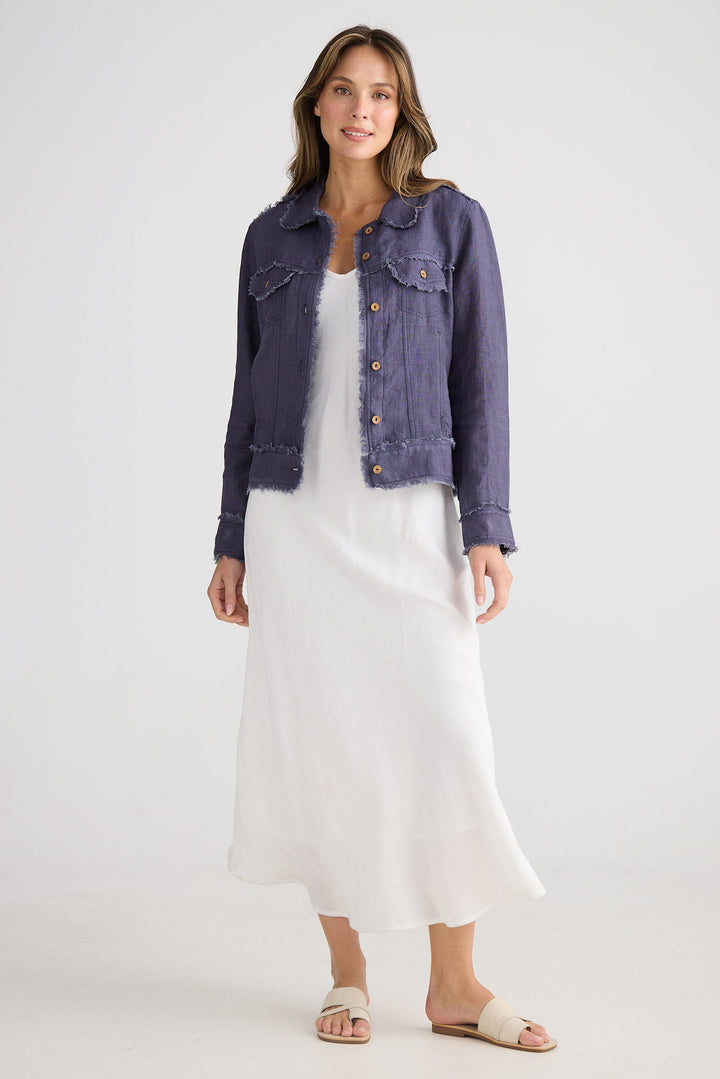 Woman wearing a navy jacket over a white dress on a plain background