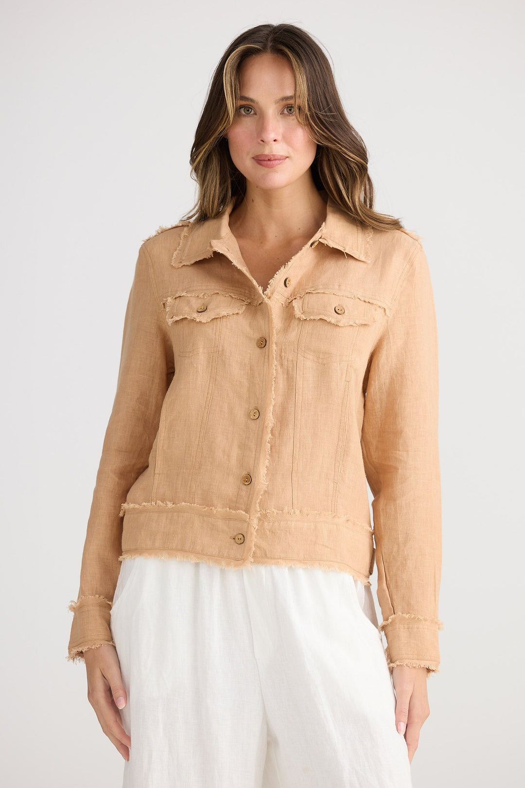 Woman wearing a beige denim jacket over a white outfit on a plain background