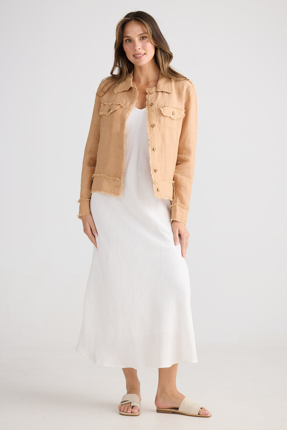Woman wearing a beige jacket over a white dress on a plain background