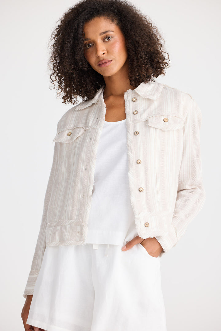 Woman wearing a light-coloured jacket over a white shirt on a plain background