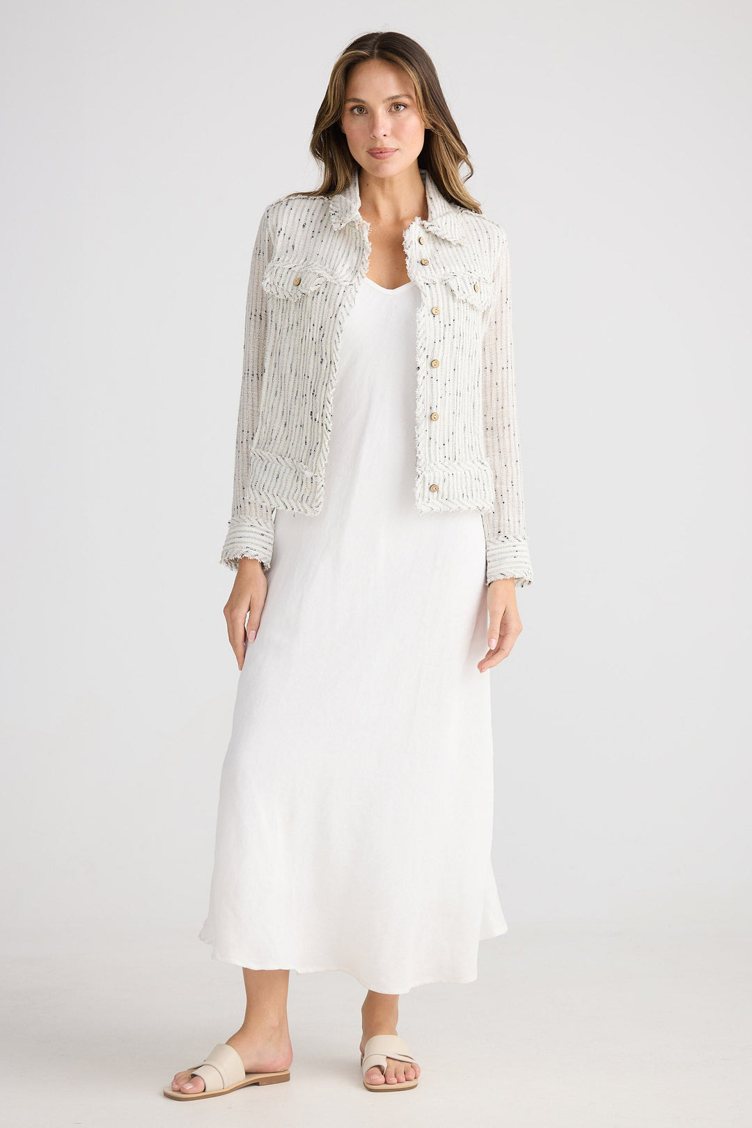 Woman wearing a white dress with a light jacket on a plain background