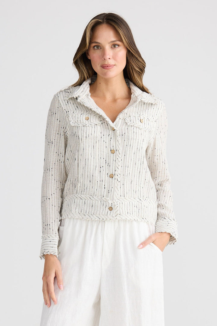 Woman wearing a light-colored cardigan and white pants on a plain background