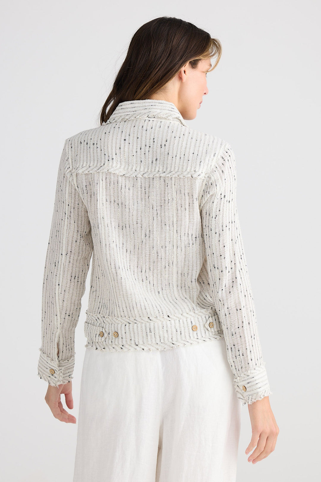 Woman wearing a light-colored lace top and white pants on a plain background