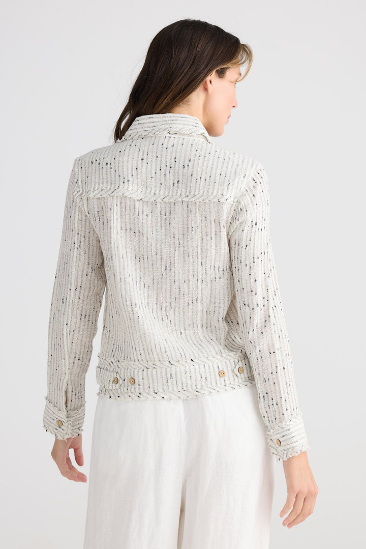 Woman wearing a light-colored lace top and white pants on a plain background