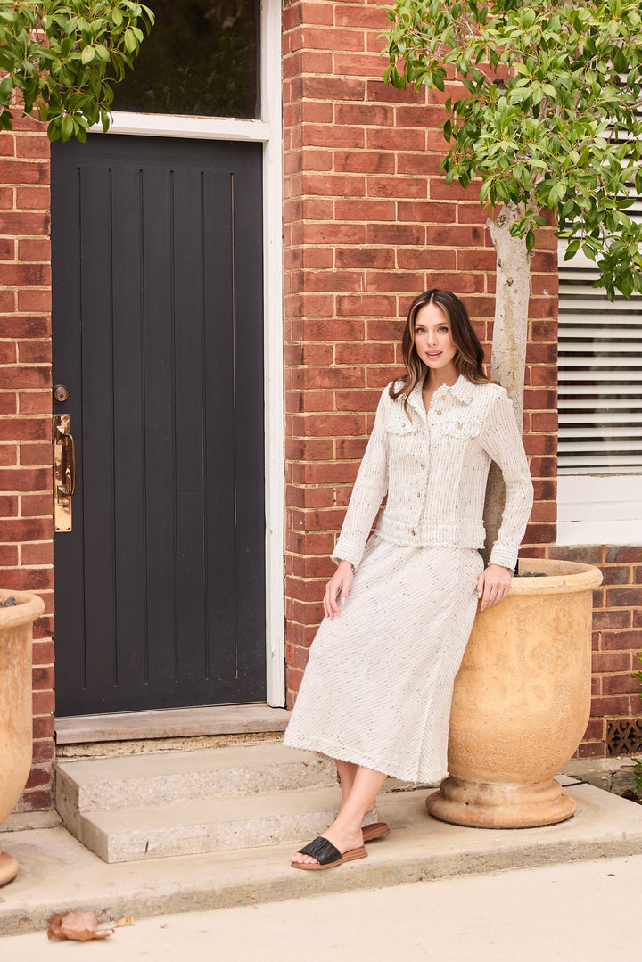 Woman standing on a porch in front of a brick building with decorative urns.