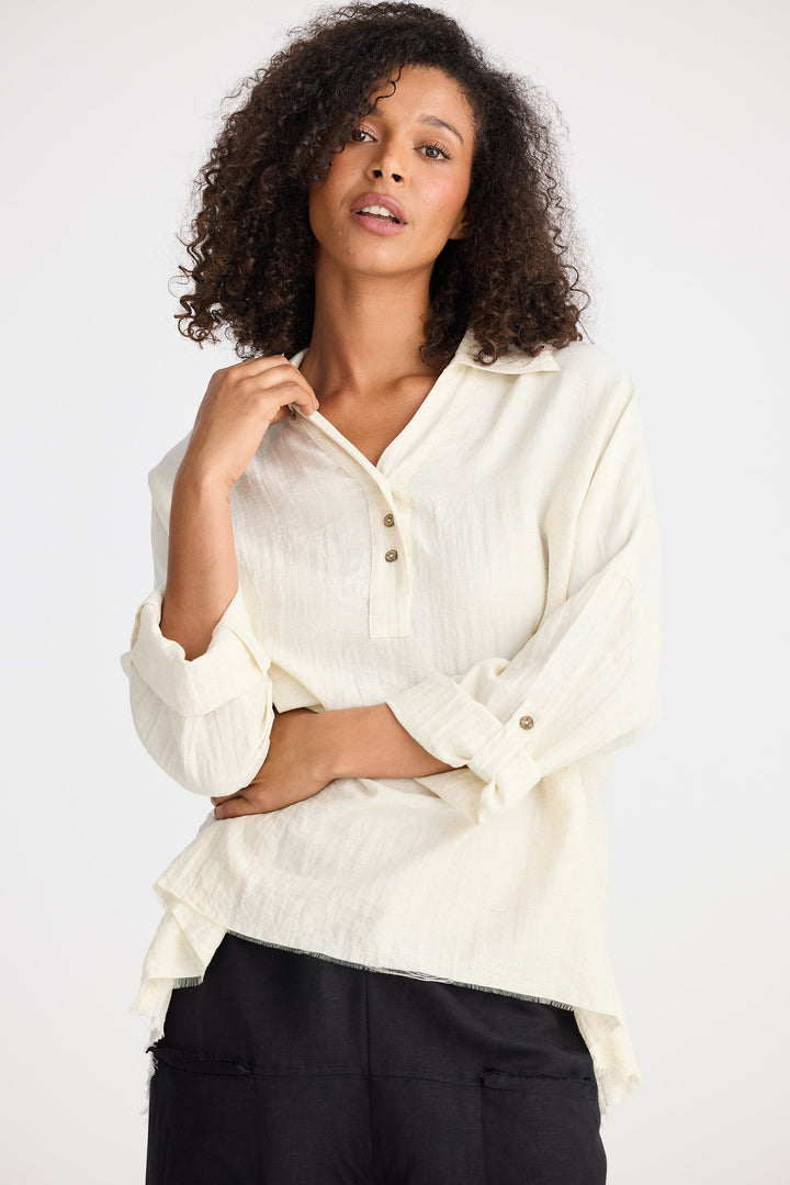 Woman wearing a white blouse with rolled-up sleeves against a plain background