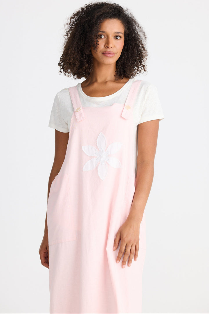 Woman wearing a light pink dress with a white flower design on a plain background