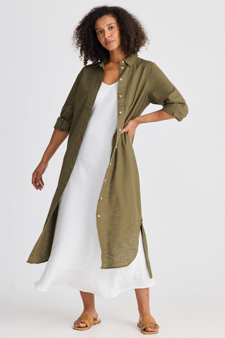 Woman wearing a long green shirt over a white dress on a white background