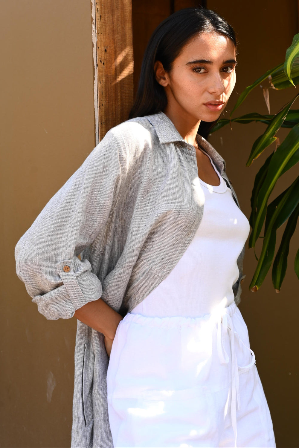 Person wearing a light gray shirt over a white dress with a plant in the foreground.