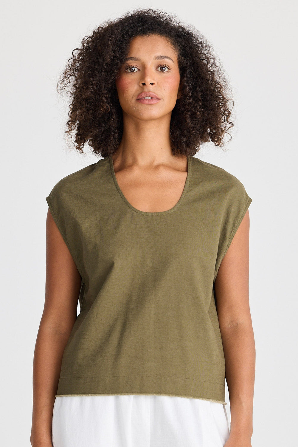 Woman wearing a green sleeveless top and white pants on a plain background