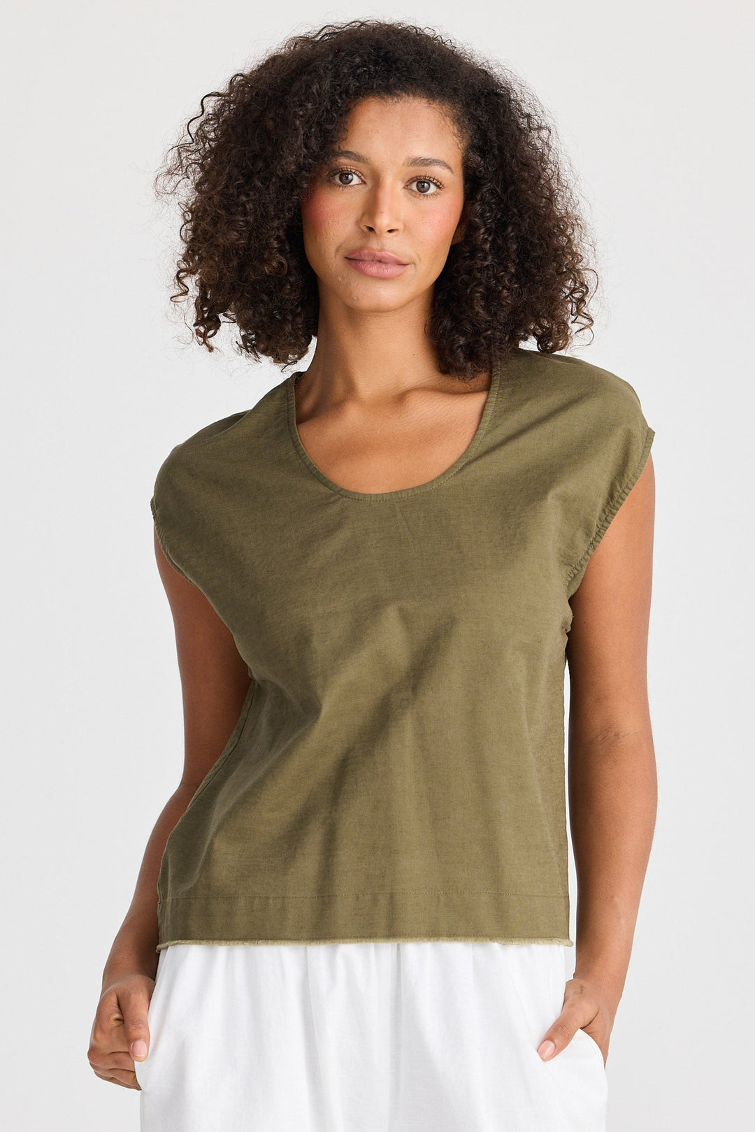 Woman wearing a green sleeveless top and white pants on a light gray background