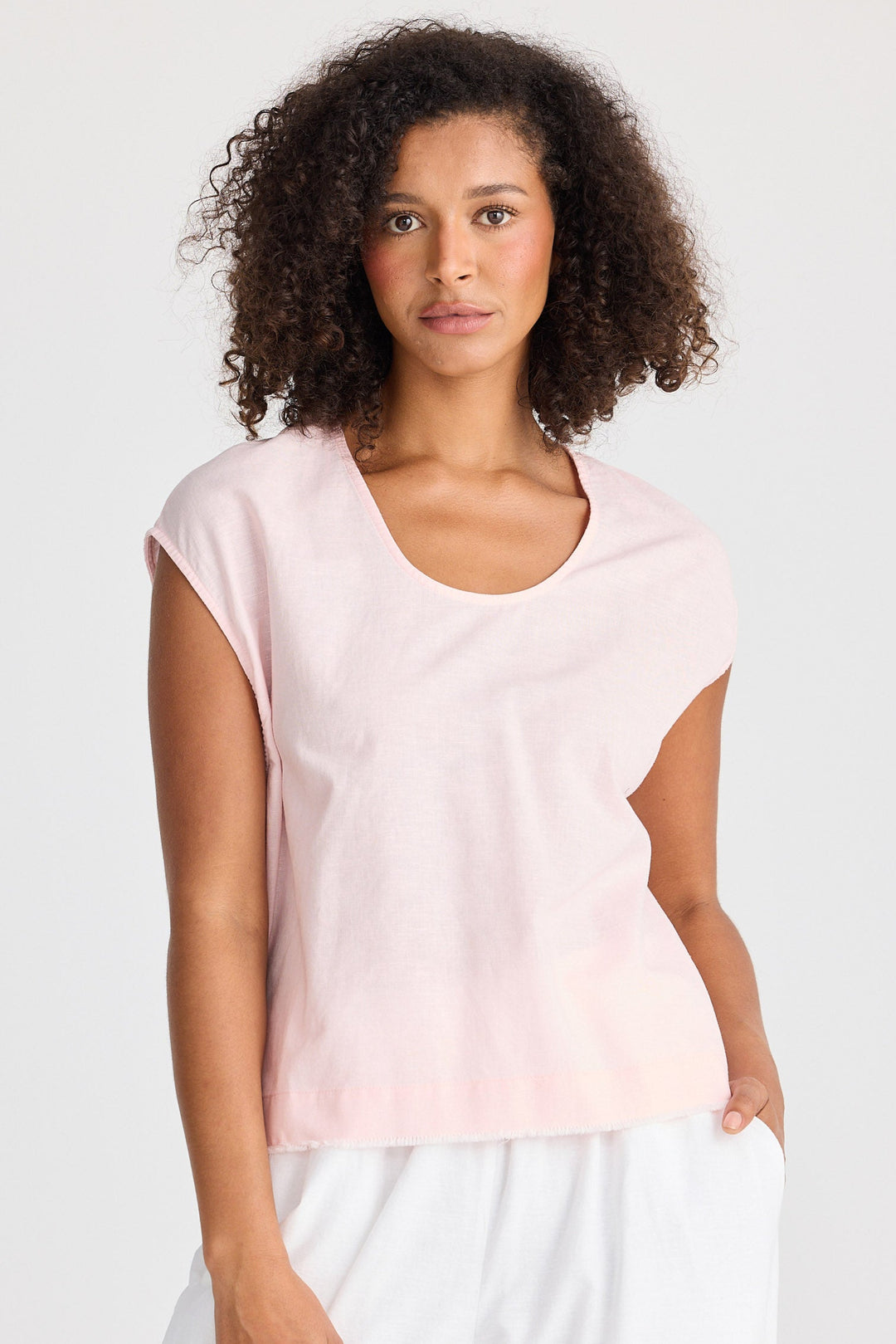 Woman wearing a light pink top and white pants on a plain background