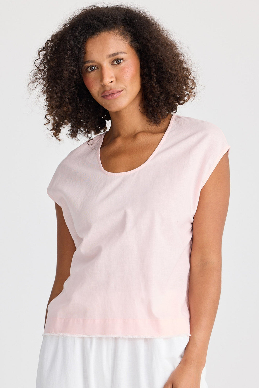 Woman wearing a light pink sleeveless top and white pants on a plain background