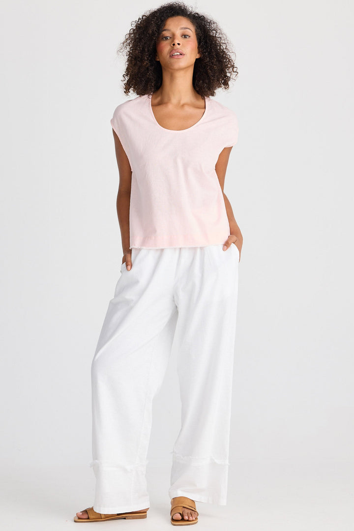 Woman wearing a light pink sleeveless top and white pants on a white background