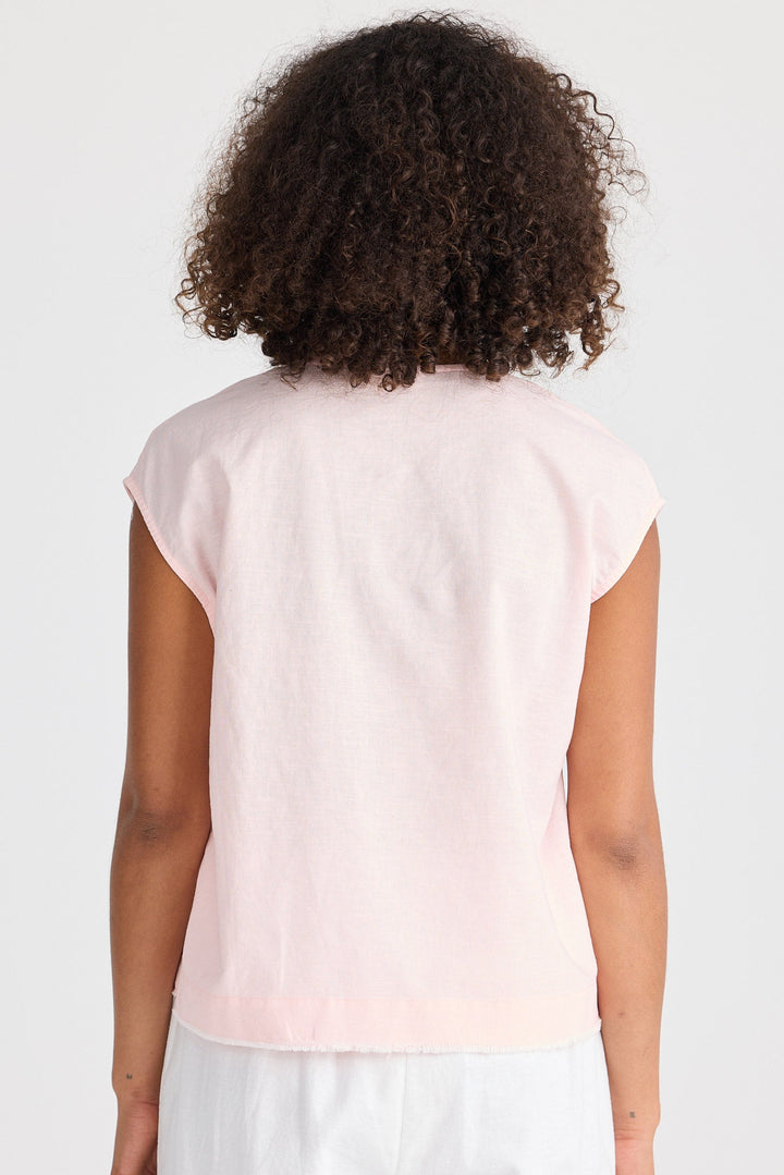 Person wearing a light pink sleeveless top and white pants on a plain background