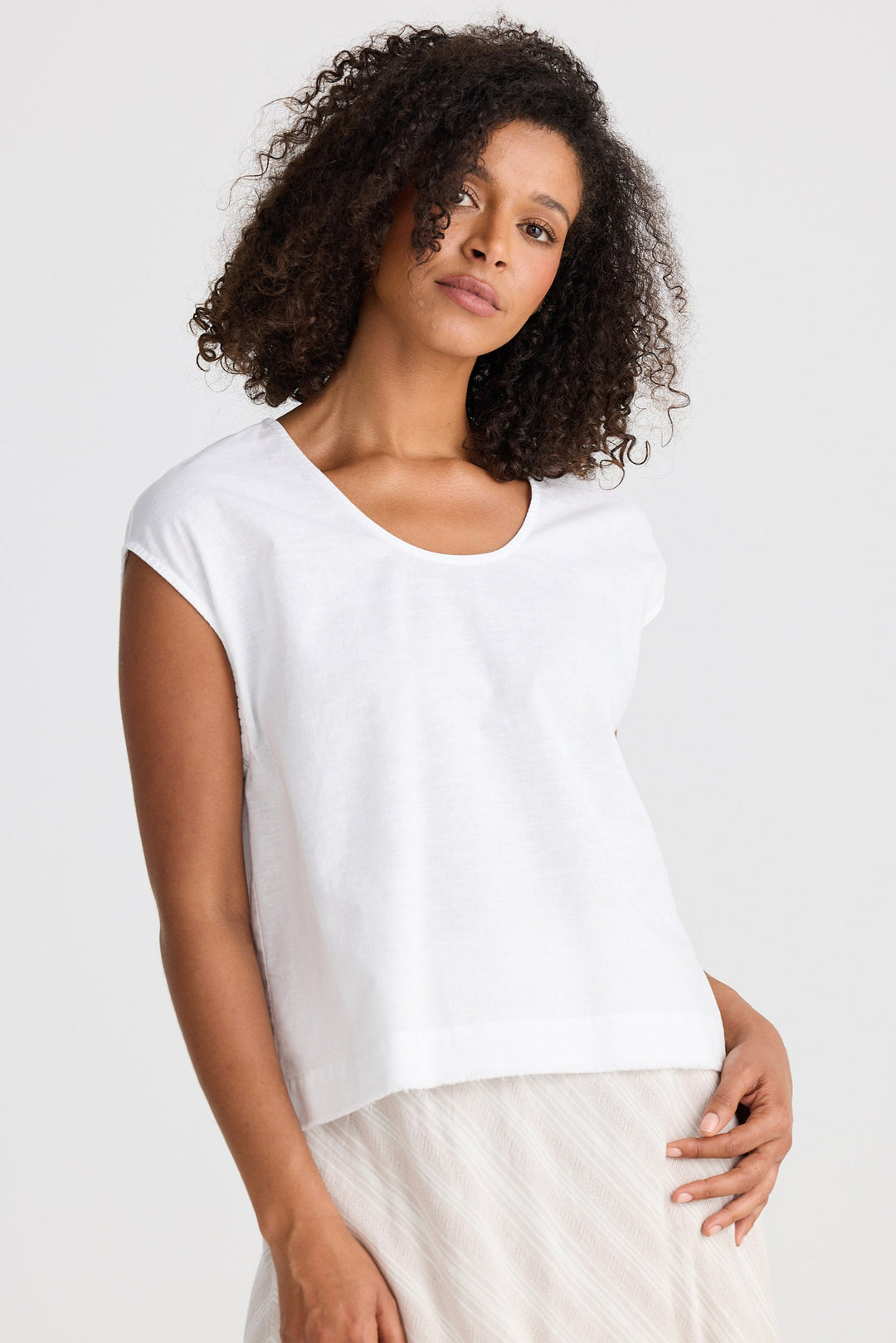 Woman wearing a white top and a light-coloured skirt against a plain background