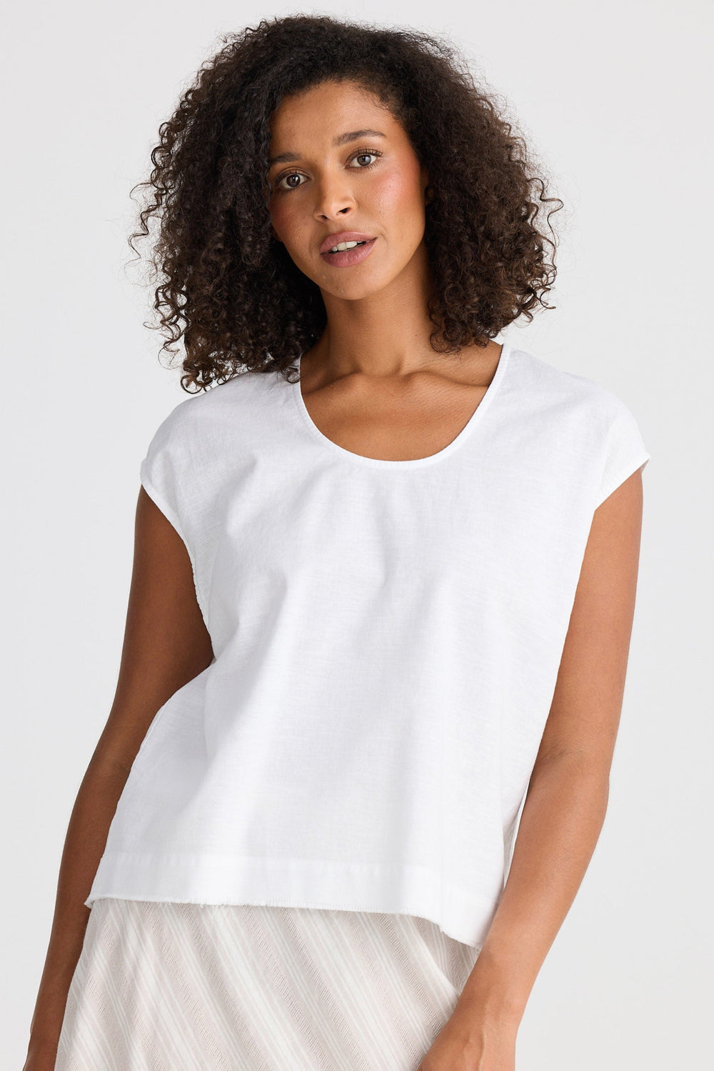 Woman wearing a white top and a light-coloured skirt against a plain background