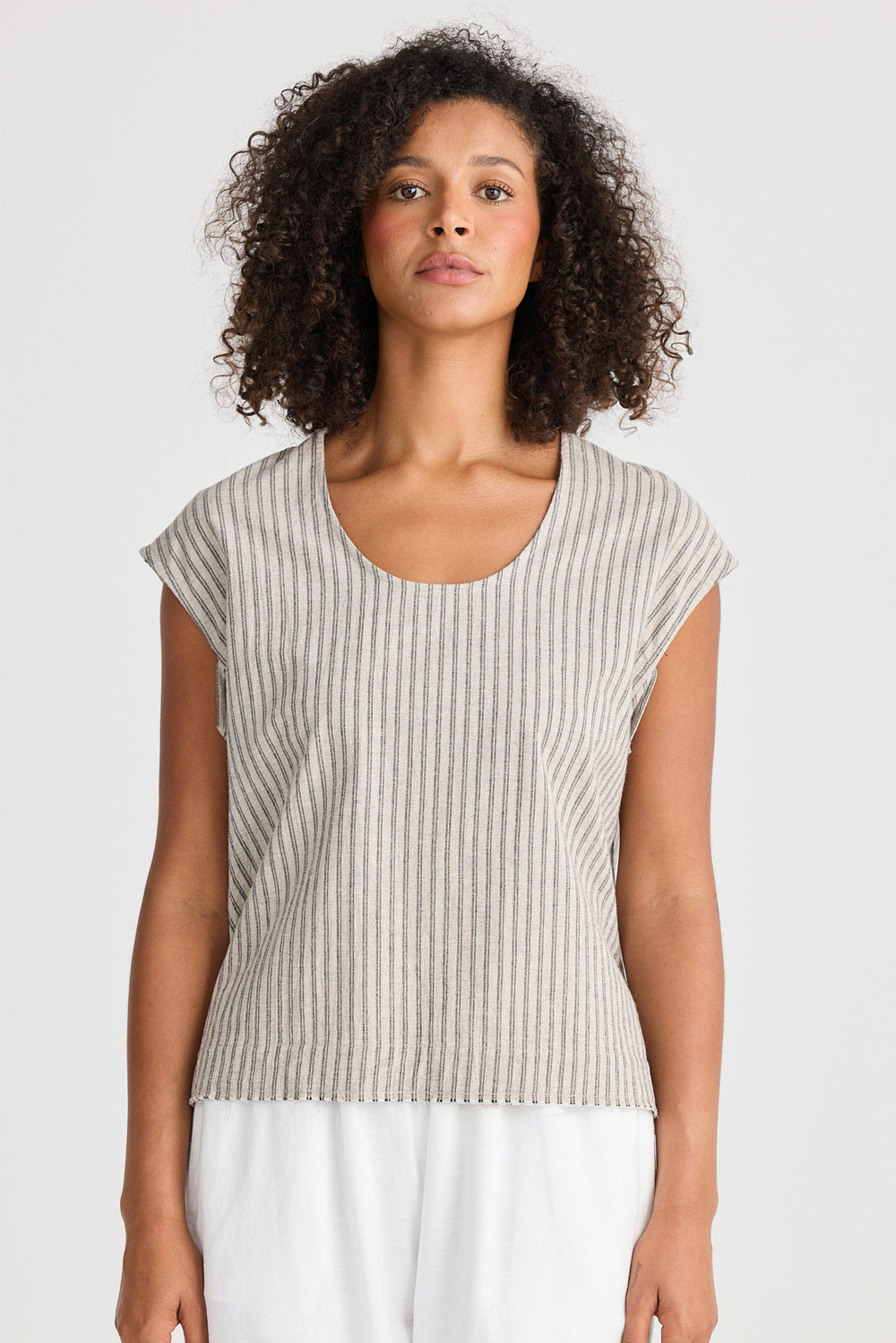 Woman wearing a striped sleeveless top and white pants on a plain background
