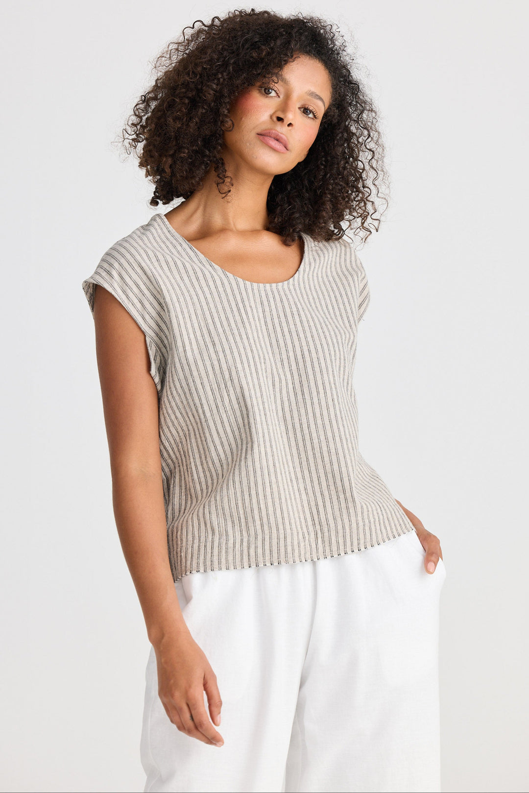 Woman wearing a beige striped top and white pants on a plain background