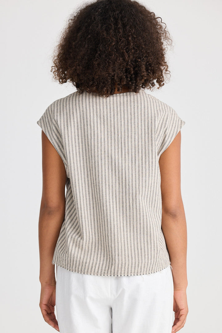 Person wearing a beige ribbed sleeveless top and white pants on a light background