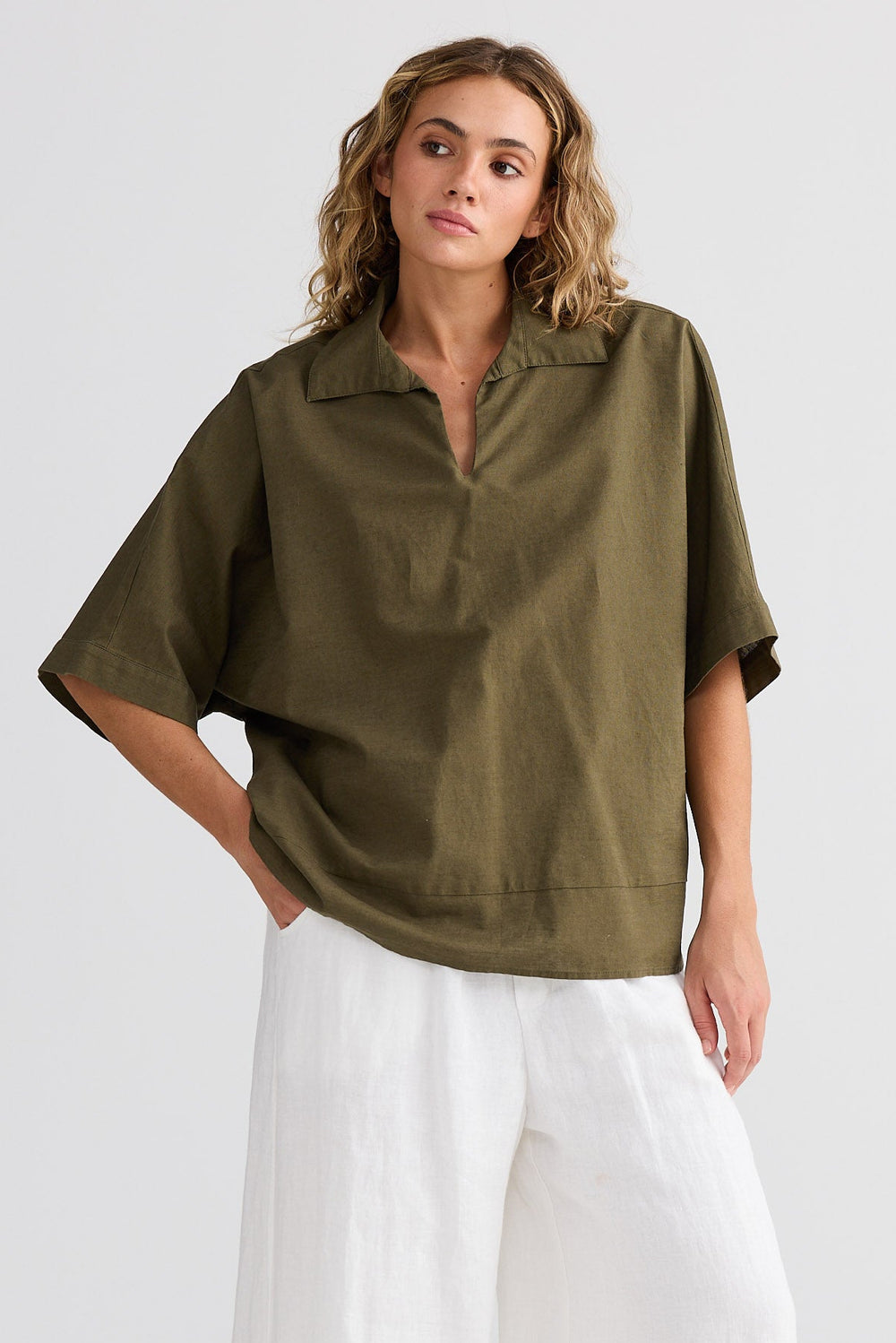 Woman wearing an olive green shirt and white pants on a white background