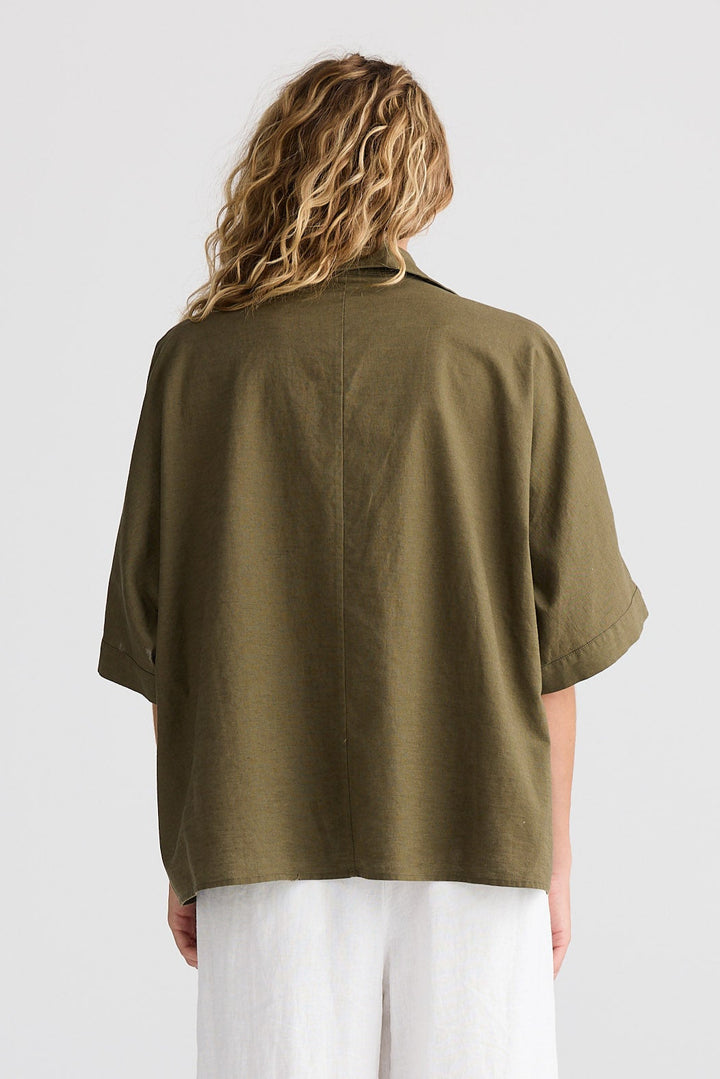 Person wearing a green oversized shirt and white pants on a white background