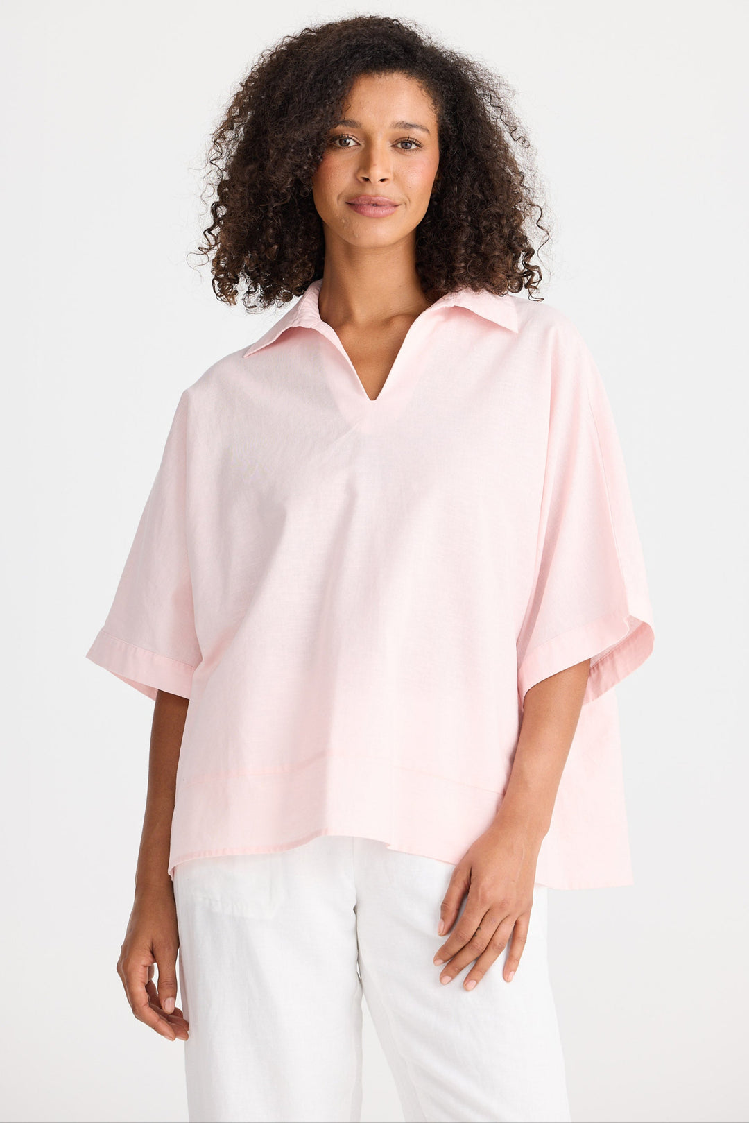 Woman wearing a light pink blouse and white pants on a white background