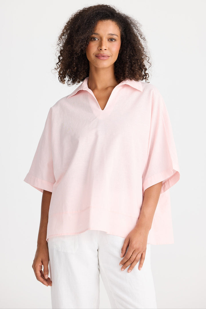 Woman wearing a light pink blouse and white pants on a white background