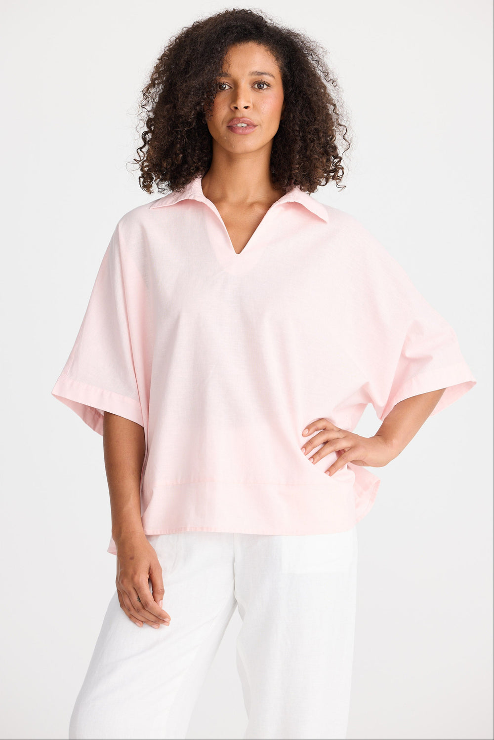Woman wearing a light pink blouse and white pants on a white background