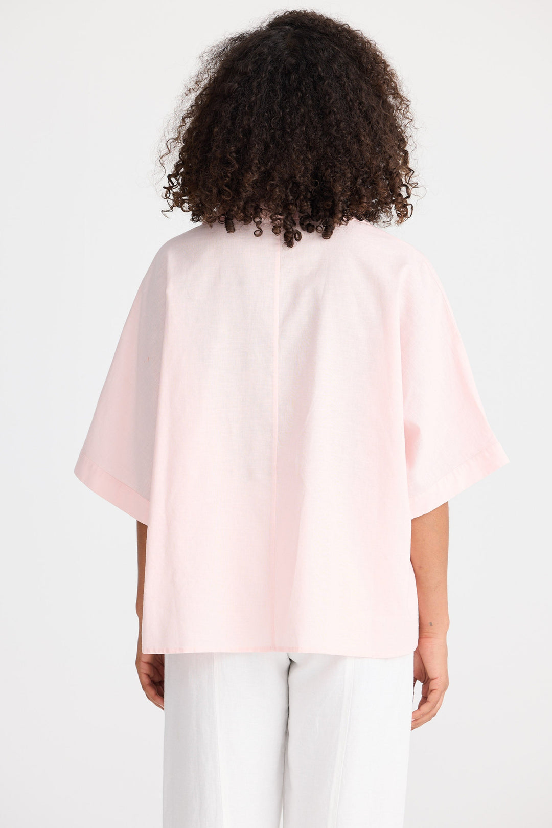 Person wearing a light pink blouse with a plain background