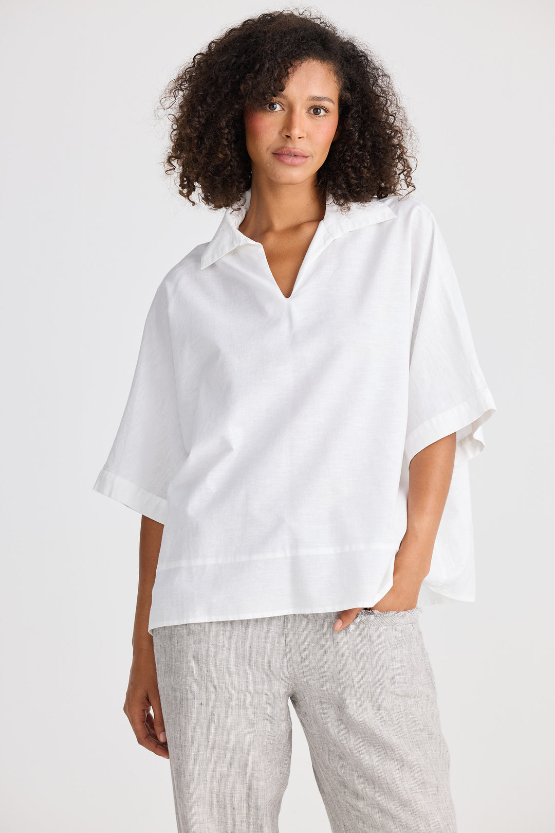 Woman wearing a white blouse and gray pants against a white background
