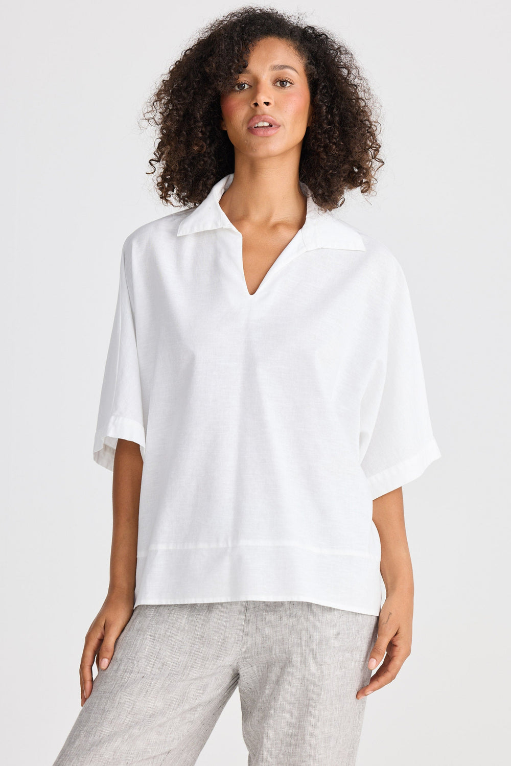 Woman wearing a white shirt and gray pants on a plain background
