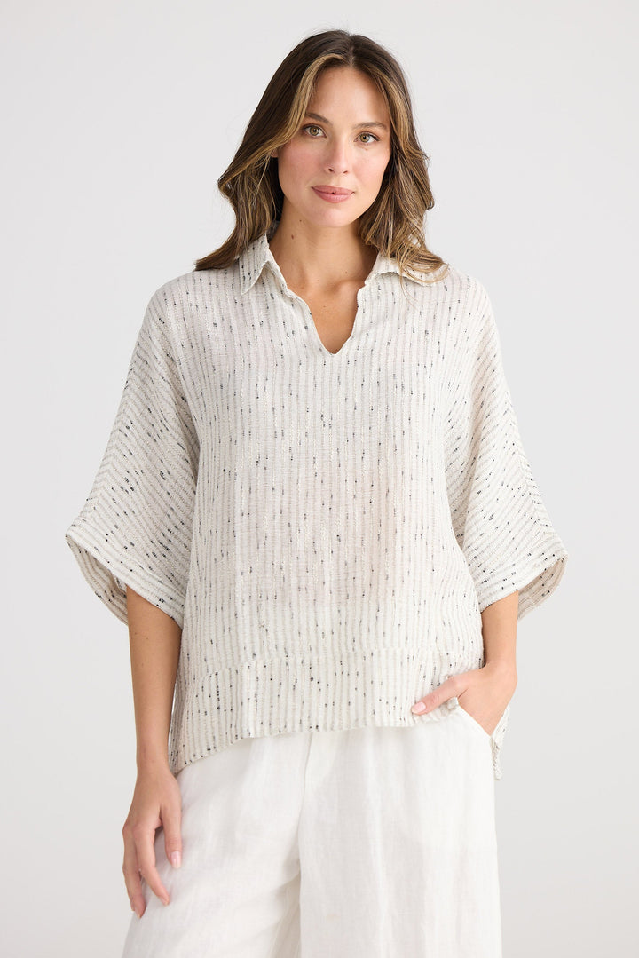 Woman wearing a light-colored blouse and white pants against a plain background