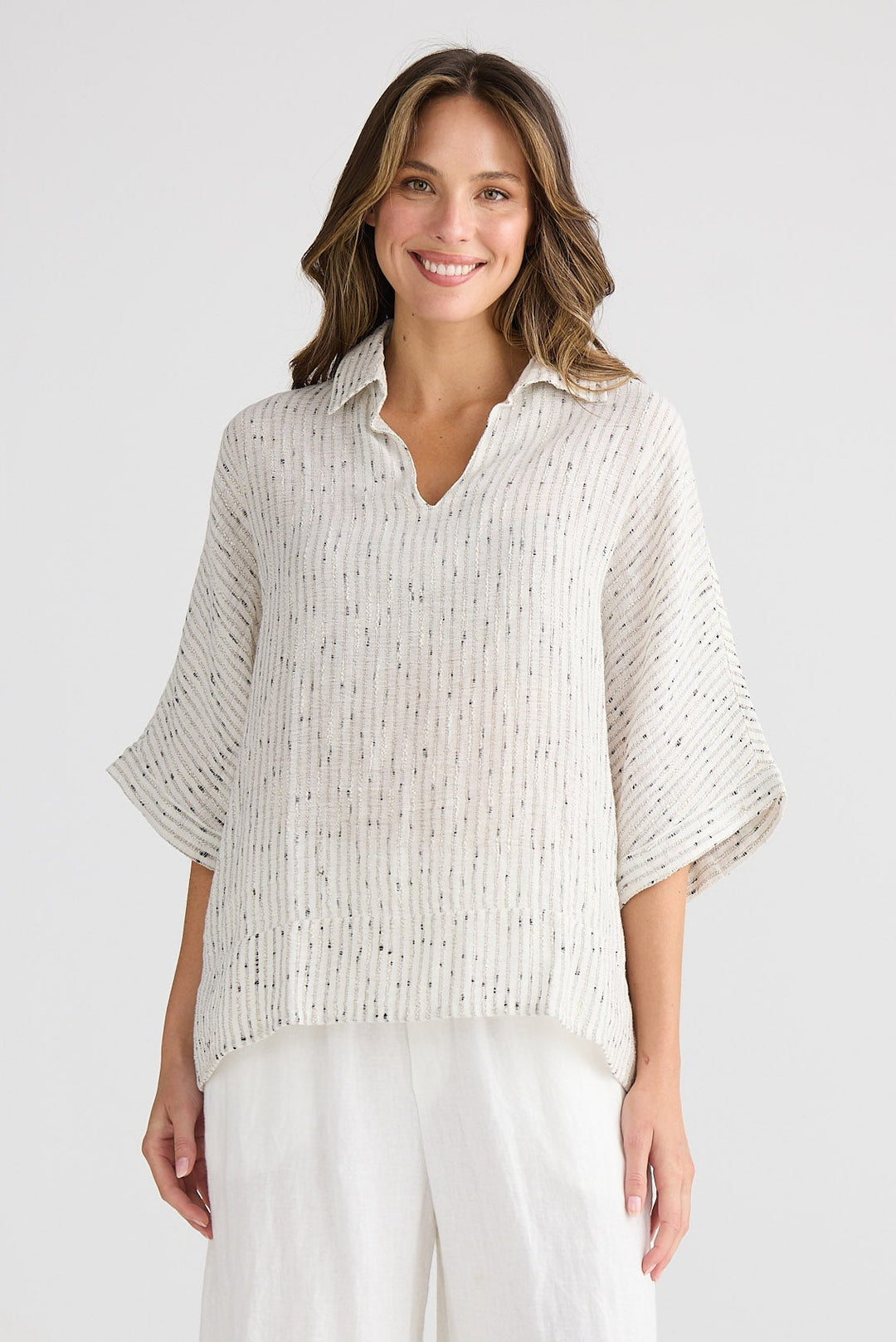 Woman wearing a light-colored blouse and white pants on a plain background