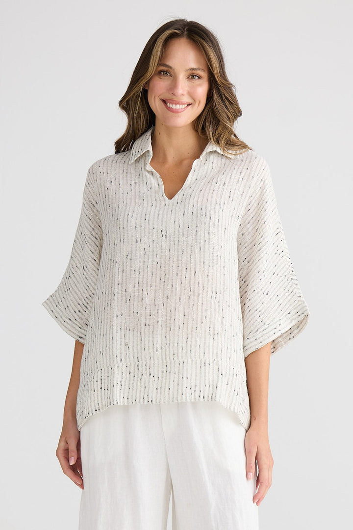 Woman wearing a light-colored blouse and white pants on a plain background