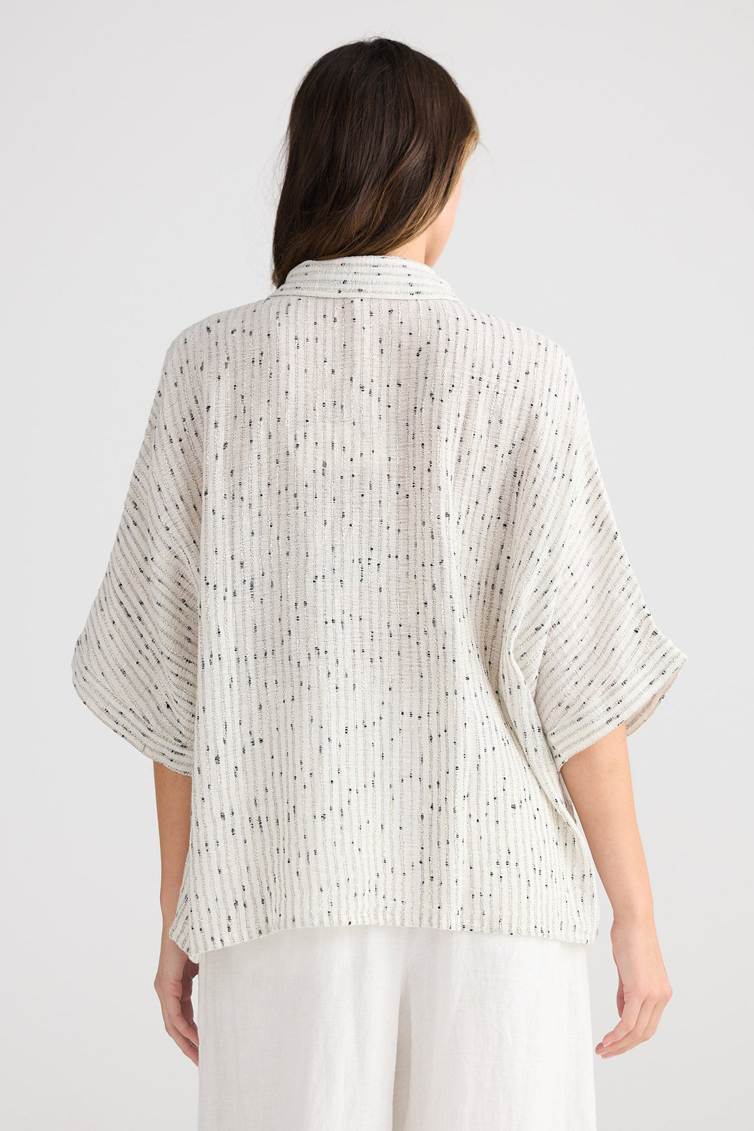 Woman wearing a light-colored textured top and white pants on a plain background