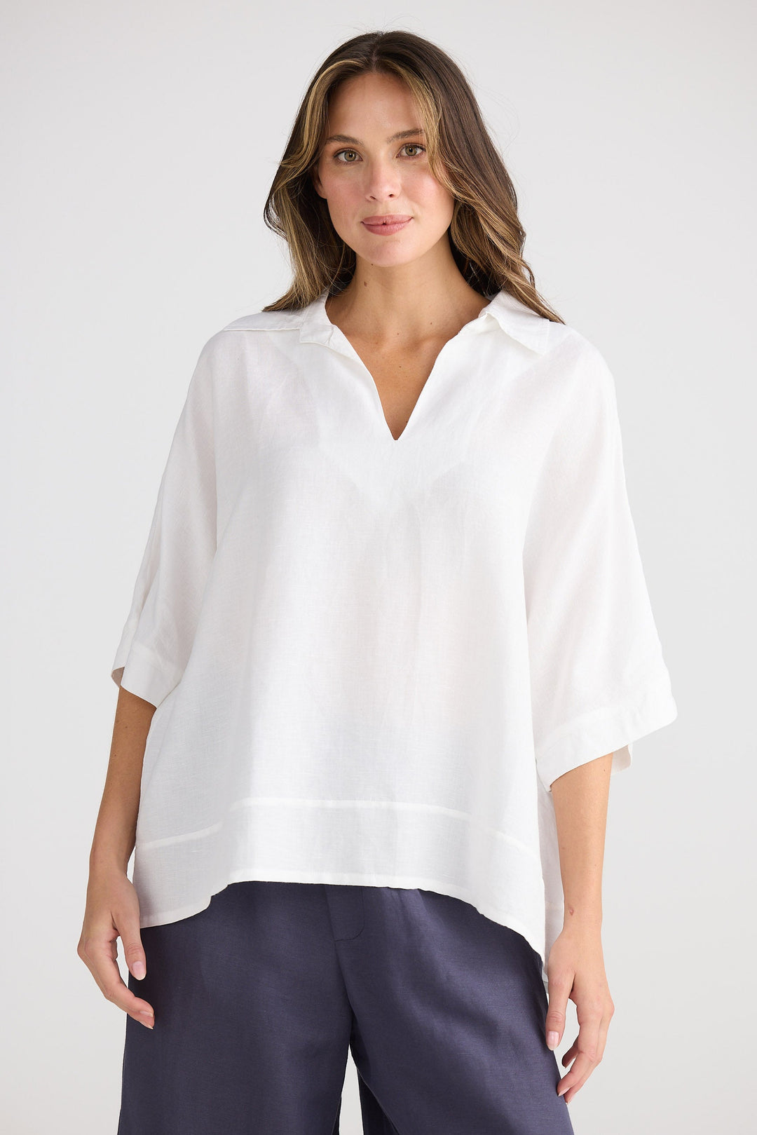 Woman wearing a white blouse and navy pants on a plain background