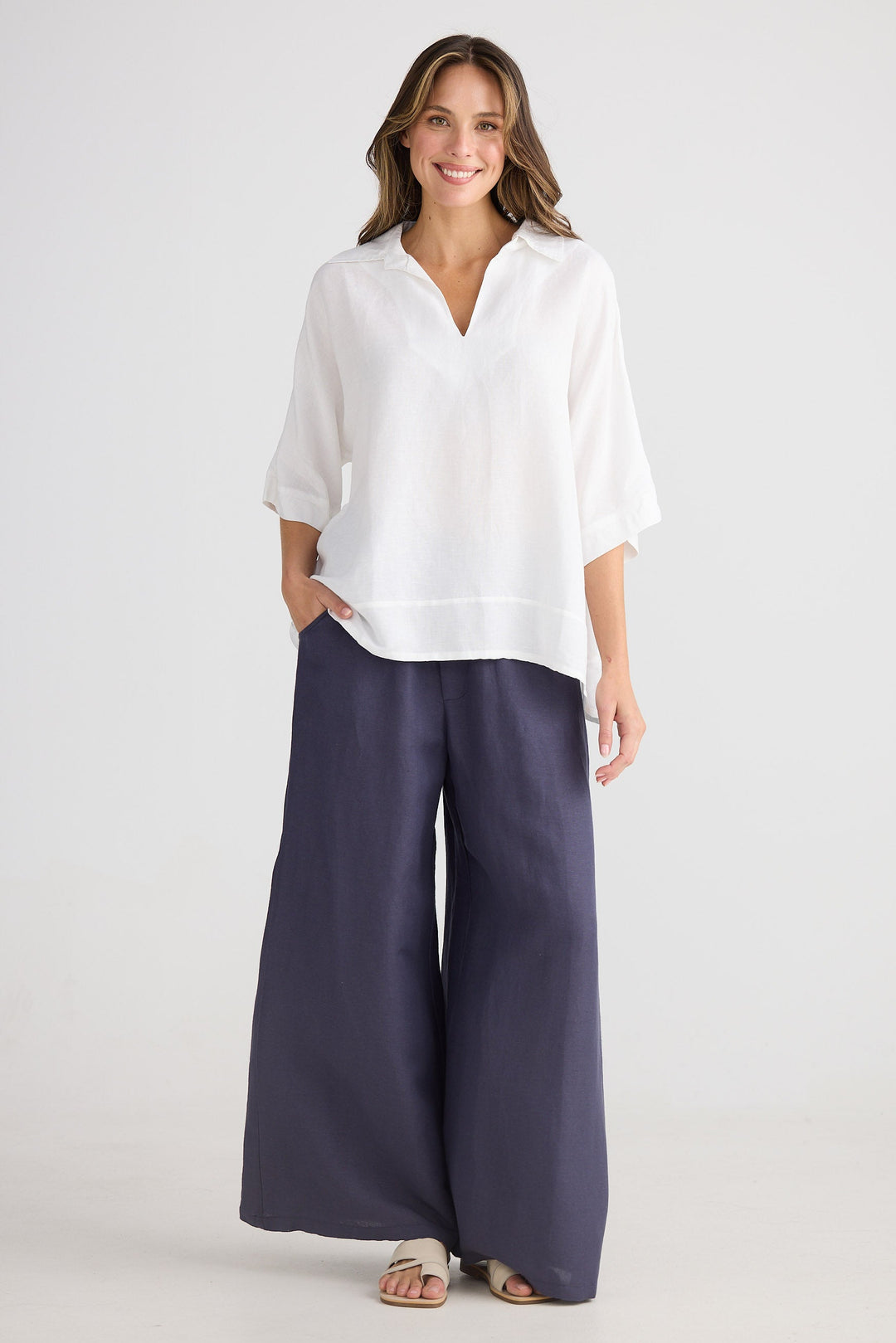 Woman wearing a white blouse and navy wide-leg pants on a white background
