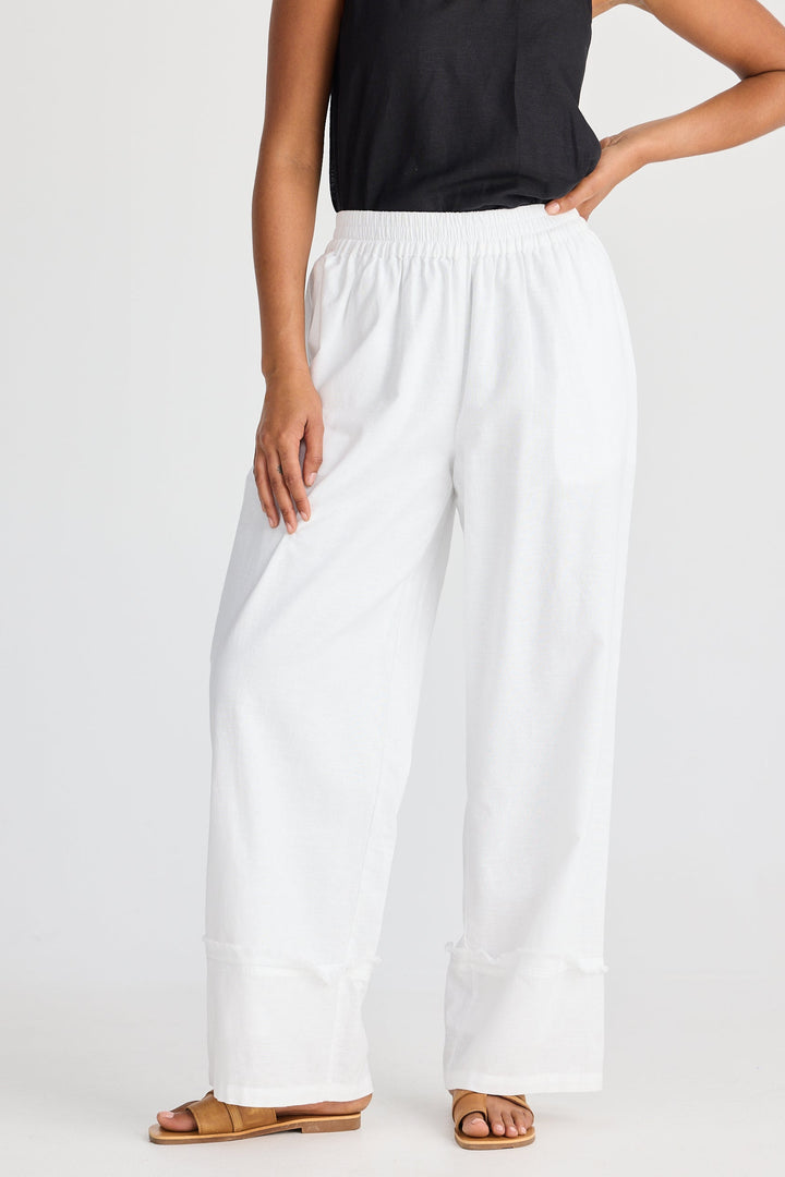 Person wearing a black tank top and white wide-leg pants on a white background
