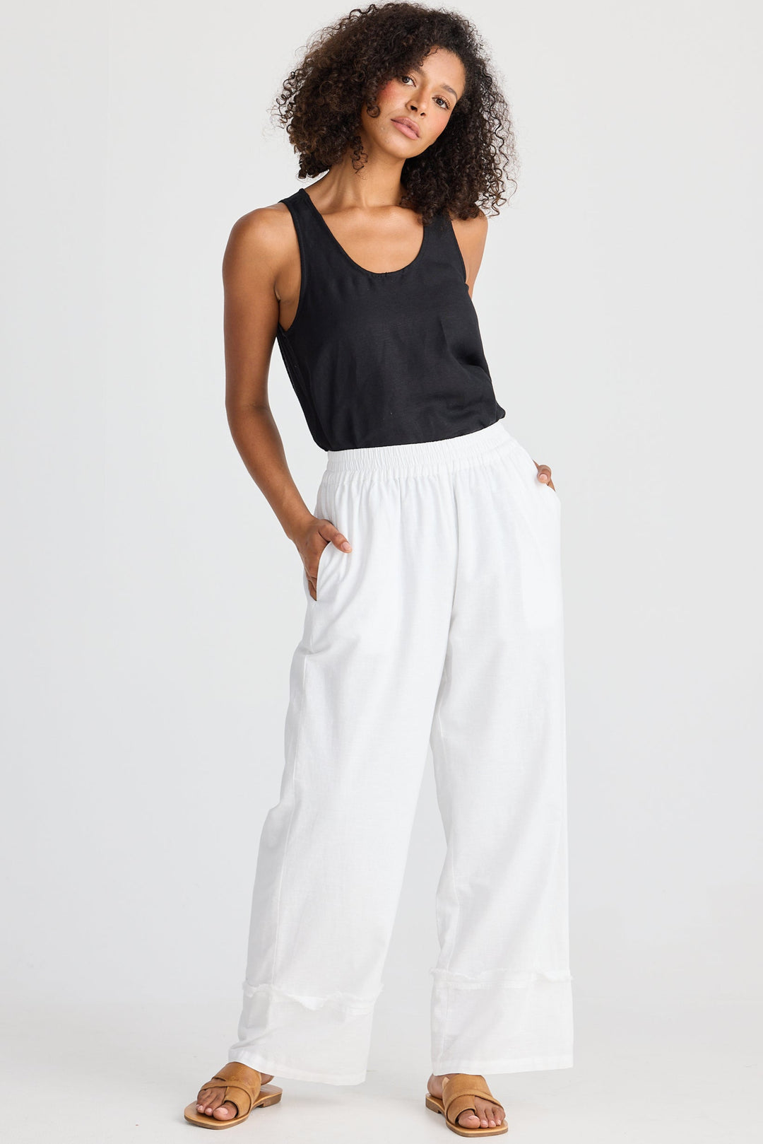 Woman wearing a black tank top and white pants on a white background