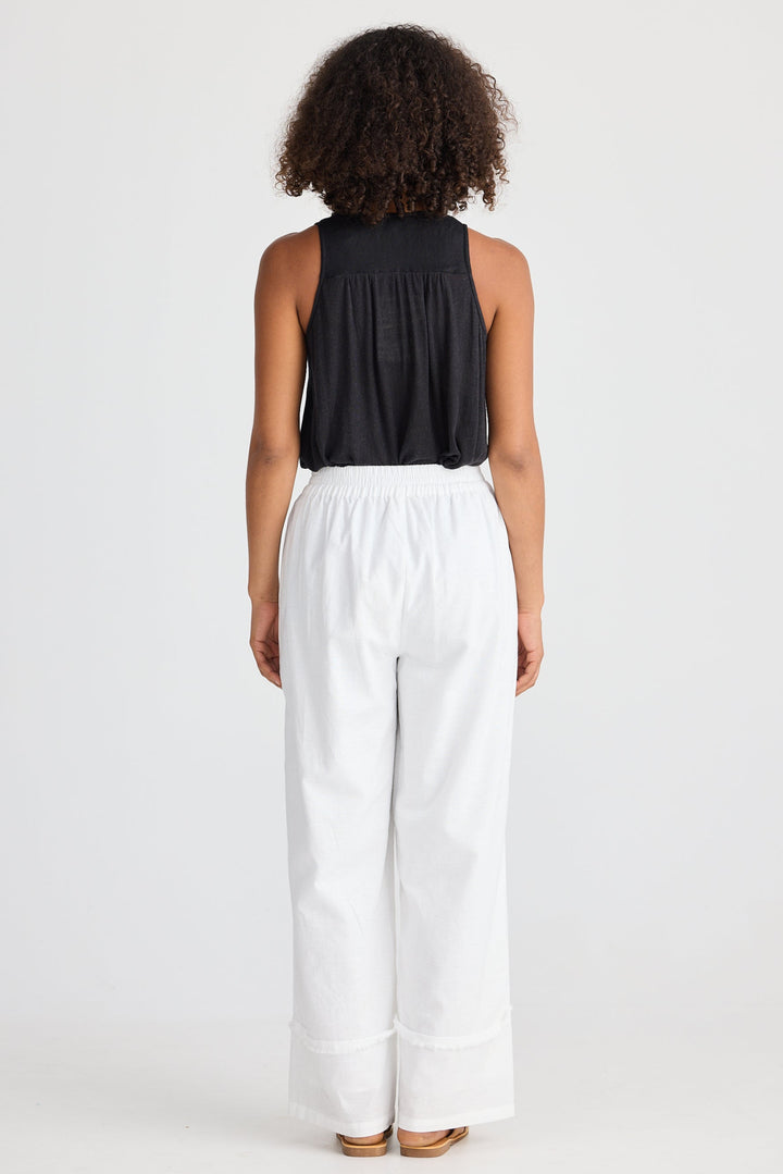 Person wearing a black sleeveless top and white pants on a white background